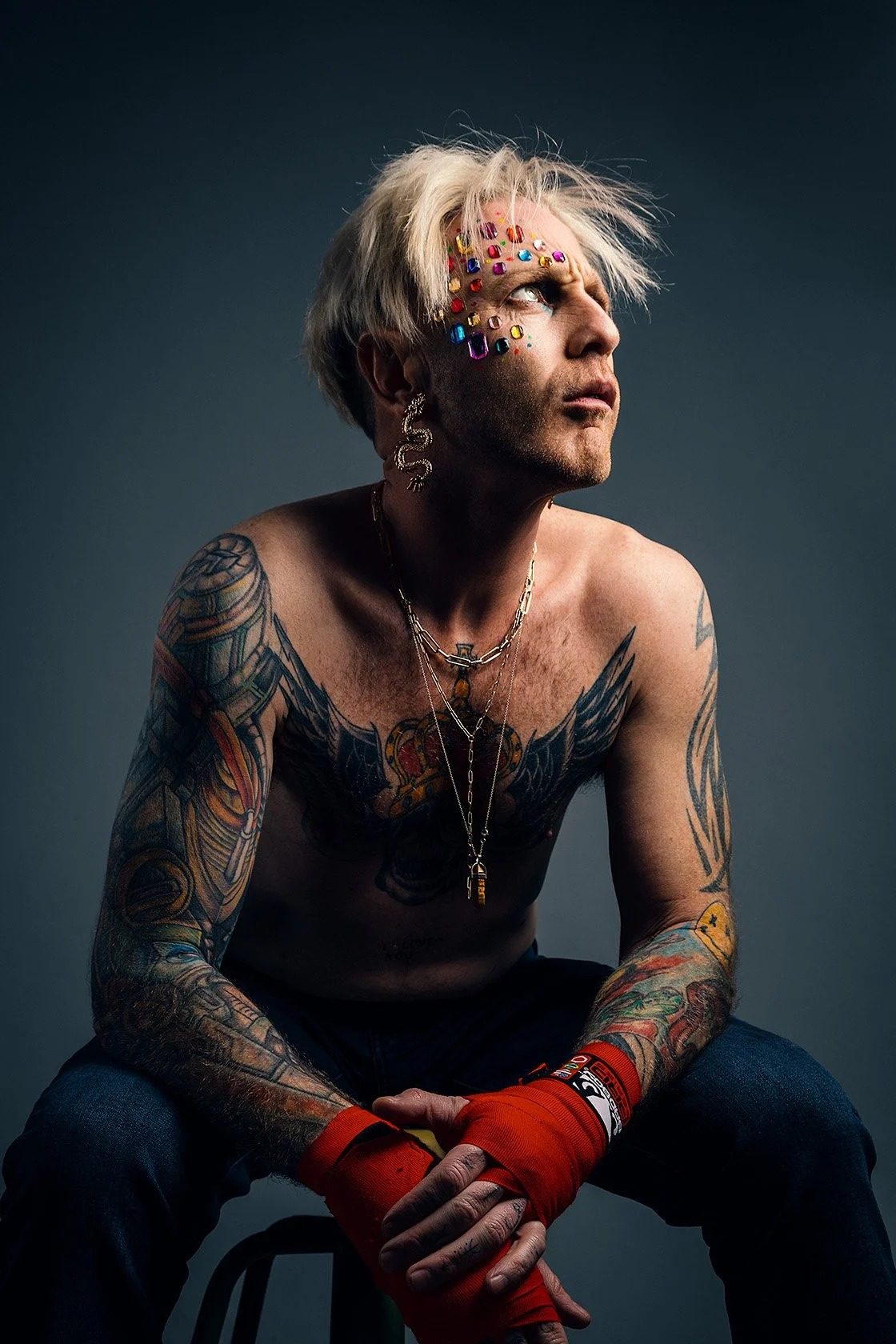 Studio portrait of tattooed man with gem-studded face